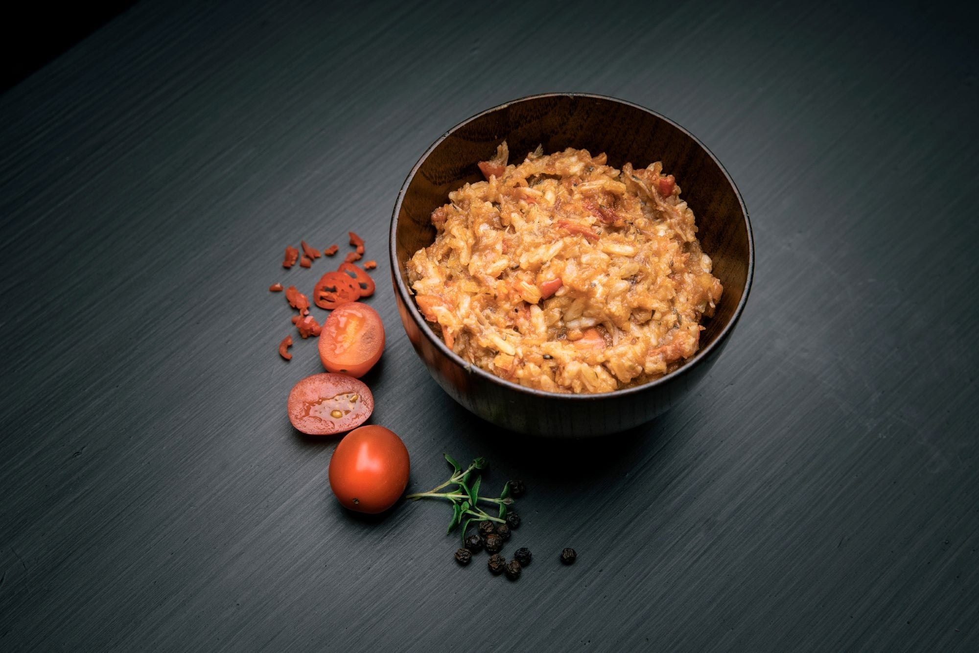 Bowl of pulled pork with rice on a dark surface with tomatoes and herbs