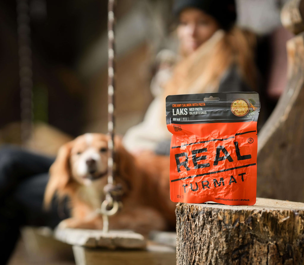 Real Turmat Creamy Salmon with Pasta
 package on a wooden stump with a dog in the background