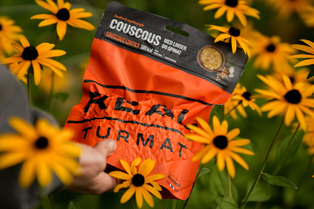 Couscous package with 'Real Turmat' branding held by a person among yellow flowers.