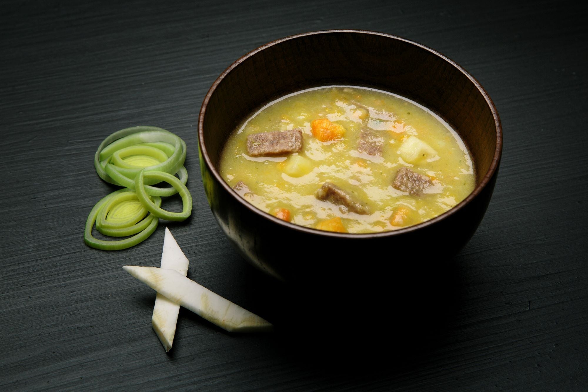 Bowl of Real Turmat Beef Soup with vegetables on a dark surface