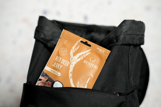 Package of red deer jerky on a black jacket with a blurred background