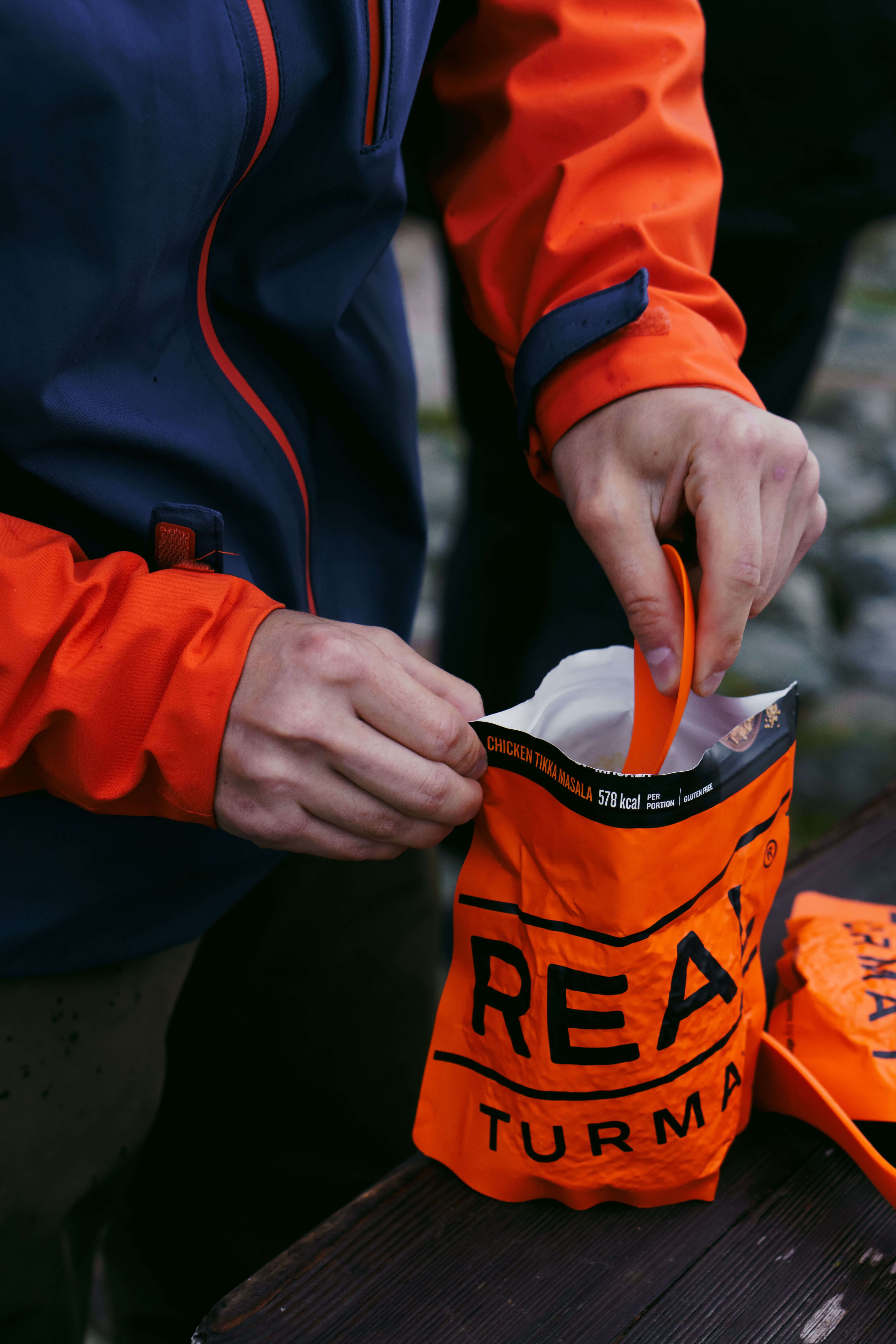 Person opening an orange Real Turmat Chicken Tikka Masala bag on a wooden surface