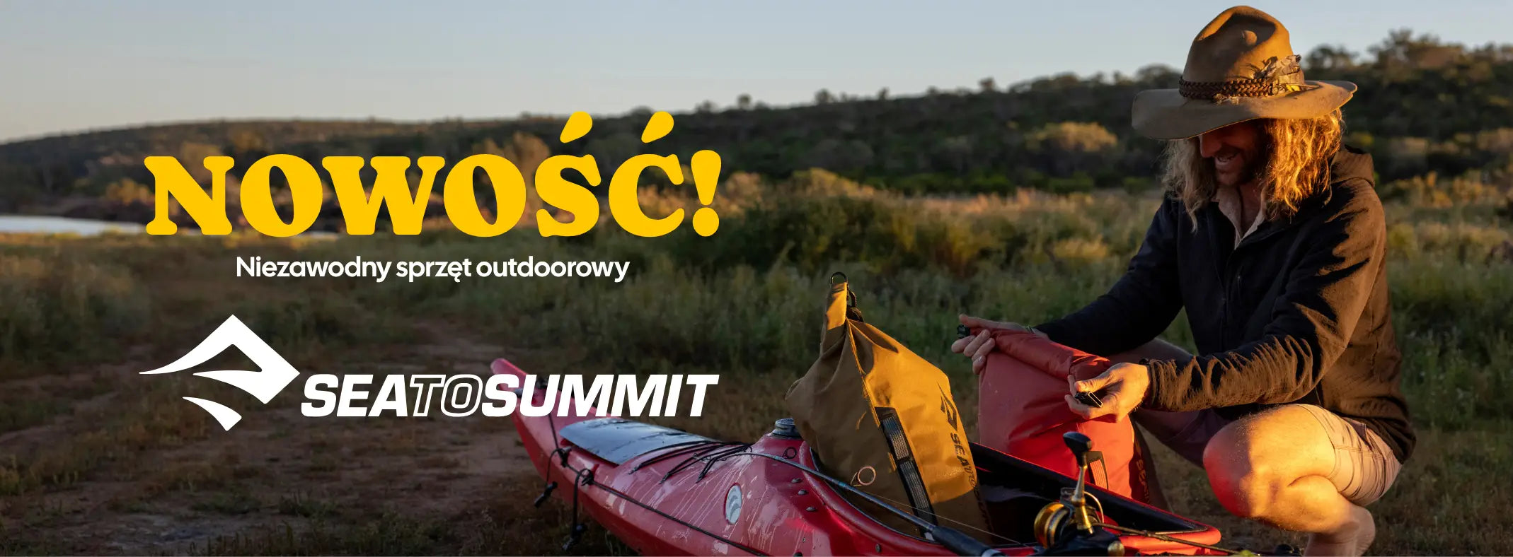 Osoba przygotowująca kajak z wyposażeniem marki Sea to Summit na tle malowniczego krajobrazu.