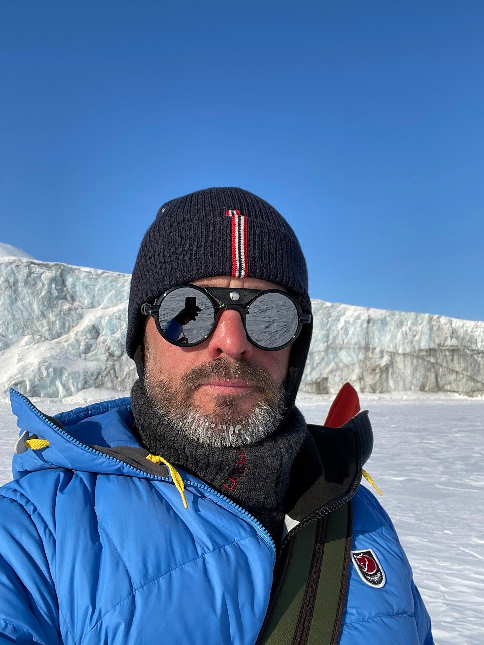 Maciej Dziurla
Traveler and outdoor enthusiast - A man wearing a blue puffer jacket, black beanie with red and white stripes, and round sunglasses takes a selfie in a snowy outdoor environment with a glacier in the background.